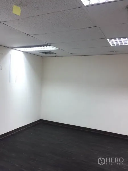 Office Space for rent in Watthana, Bangkok - Vacant office corner with white walls, dark vinyl flooring and recessed fluorescent lights.