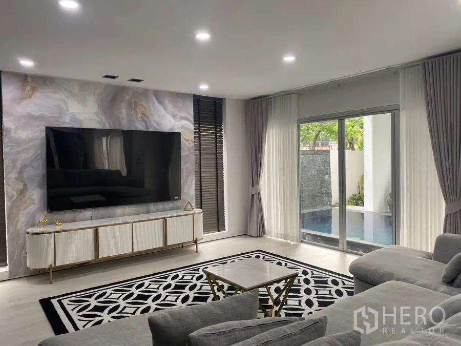 Detached House for rent in Suan Luang, Bangkok - Bright living room with a large TV on a marble feature wall and sliding doors opening to the pool.