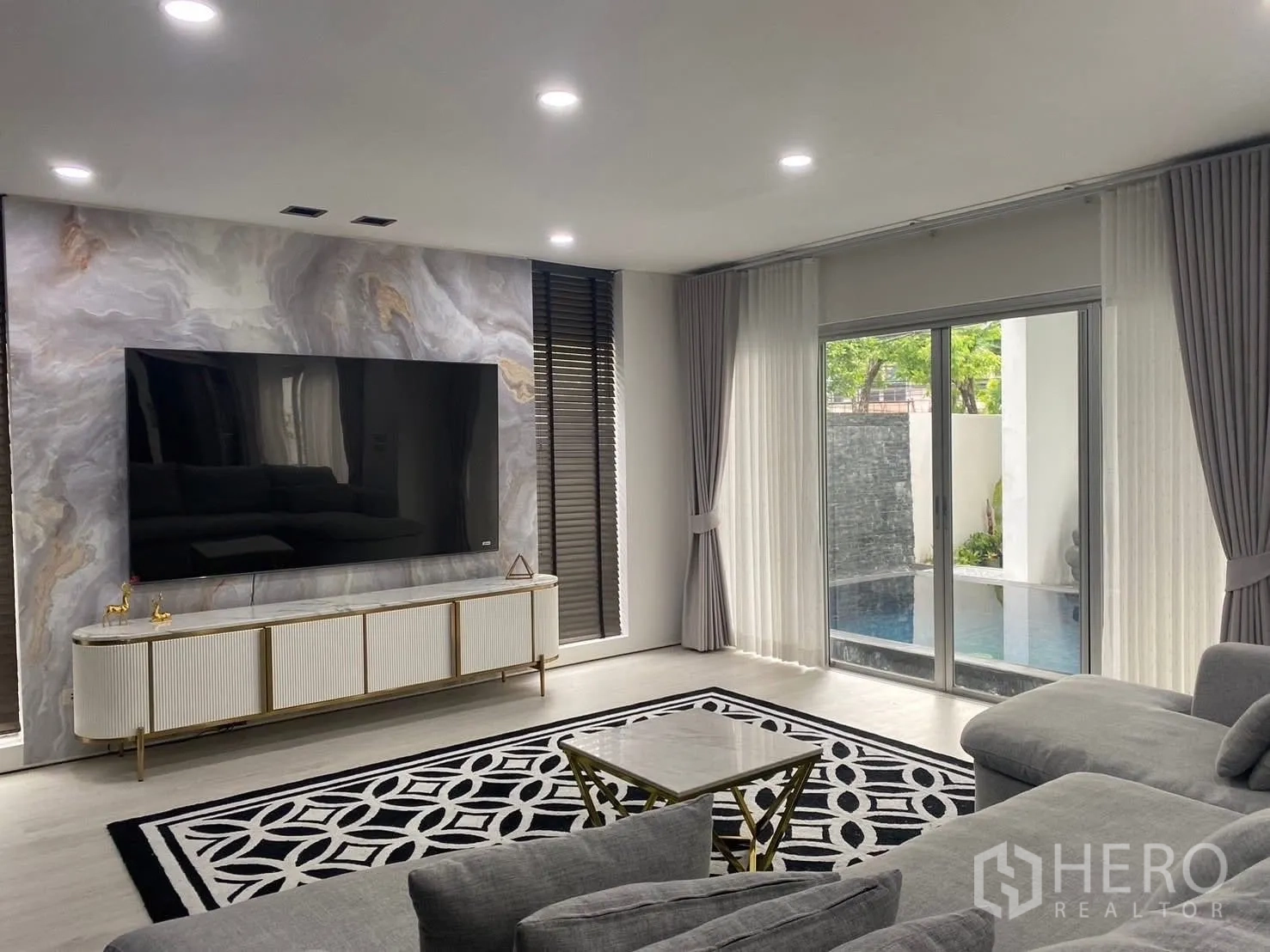 Detached House for rent in Suan Luang, Bangkok - Bright living room with a large TV on a marble feature wall and sliding doors opening to the pool.