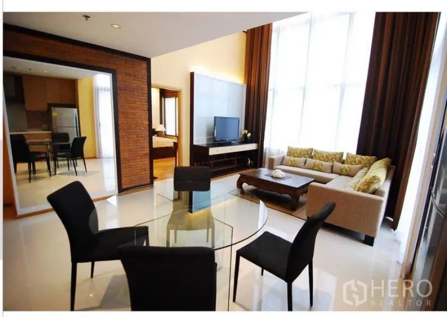 Condominium for rent - Open-plan lounge with glass dining table, TV console and tall windows with heavy curtains.
