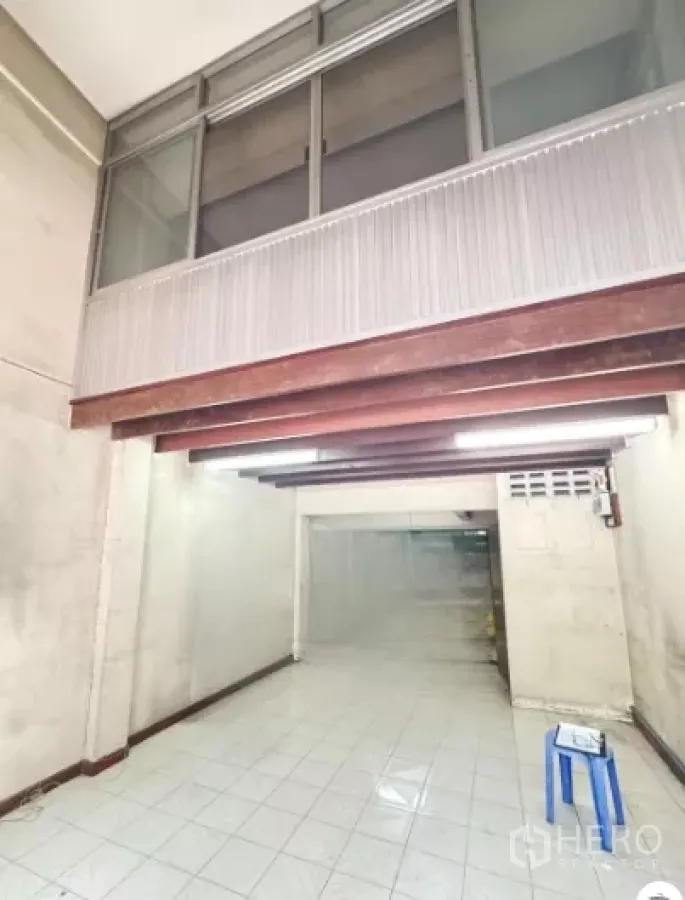 Shophouse for rent in Watthana, Bangkok - Ground-floor shop hall with white tiles, exposed wooden beams and upper glass windows.