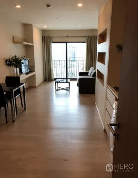 Condominium for rent in Khlong Toei, Bangkok - Entry hall leading to a sunny living room with dining table, TV console and balcony doors.