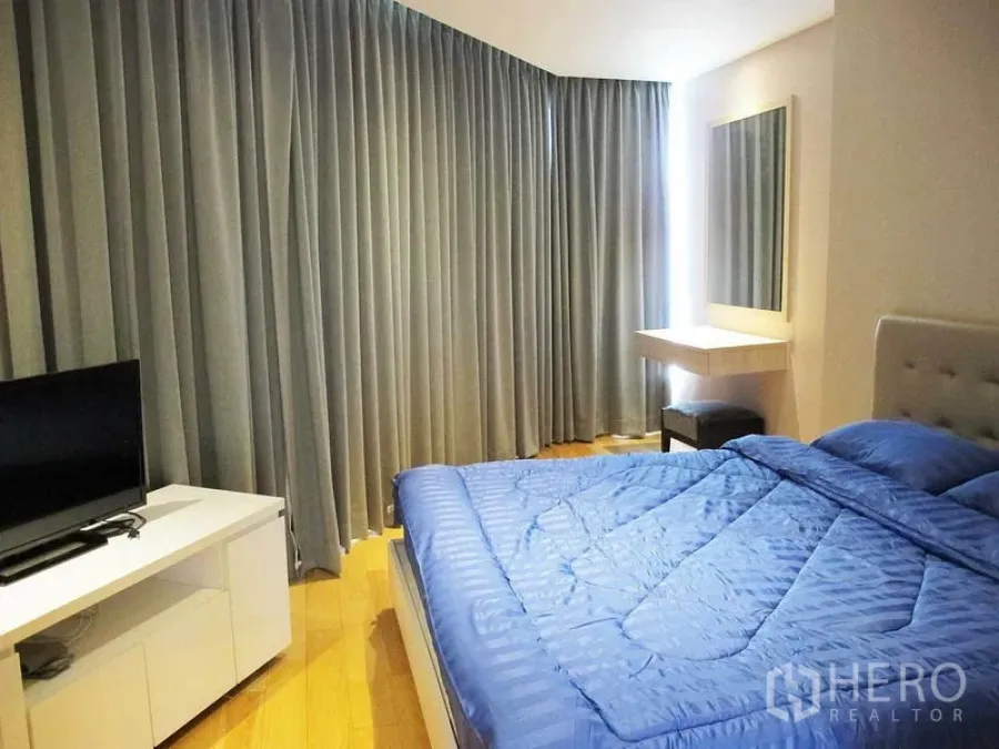 Condominium for rent in Watthana, Bangkok - Master bedroom with blue duvet, floor-to-ceiling curtains, wall mirror and TV console.