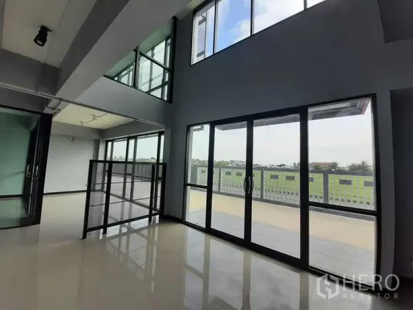 Factory for rent or sale - Double-height office space with floor-to-ceiling windows opening to a balcony and open green views.