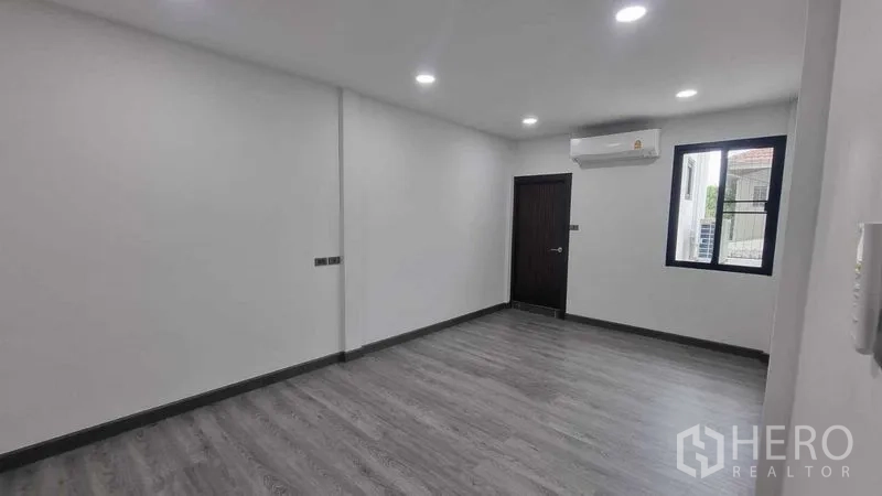 Townhouse for rent in Khlong Toei, Bangkok - Air-conditioned bedroom with gray floors, white walls, window, and dark door frames.