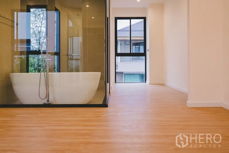 Townhouse for sale in Phra Khanong, Bangkok - Bedroom level with warm wood floors and a glass room containing a freestanding soaking tub.
