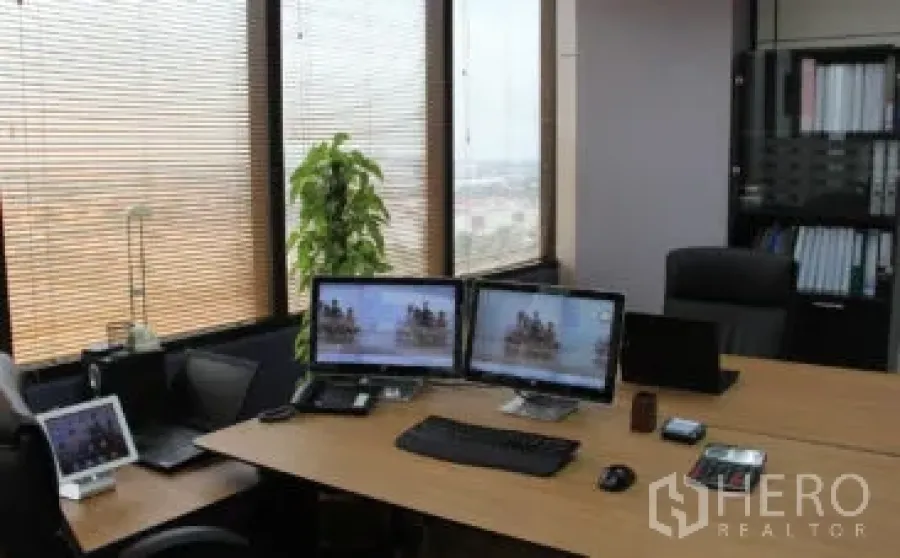 Office Space for rent in Bang Na, Bangkok - Modern workstation with dual monitors, large corner windows with blinds, city views, and filing shelves in a Bang Na office.