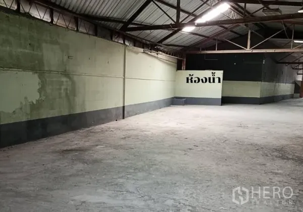 Warehouse for rent in Bang Khen, Bangkok - Open-span warehouse bay with steel trusses, painted walls and a signed restroom area.