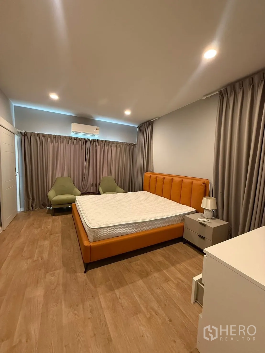 Detached House for rent in Bang Kapi, Bangkok - Spacious bedroom with an orange upholstered bed, wood flooring, grey curtains and recessed lights.