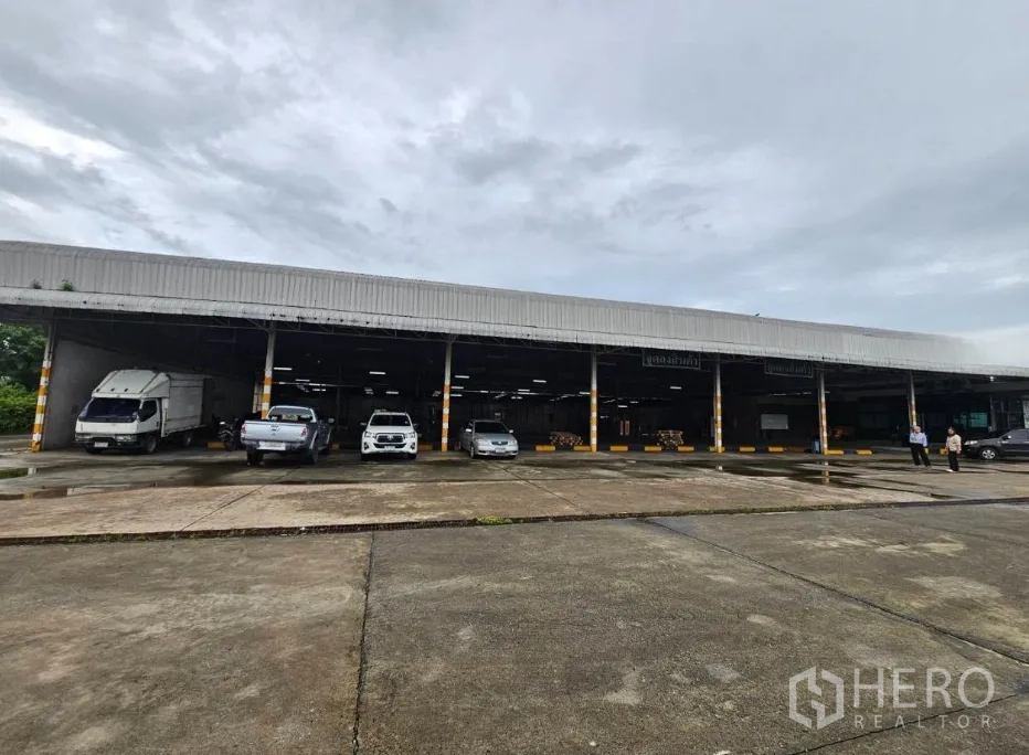 Warehouse for rent in Lam Luk Ka, Pathum Thani - Exterior of long warehouse under canopy with vehicles at dock-high bays.