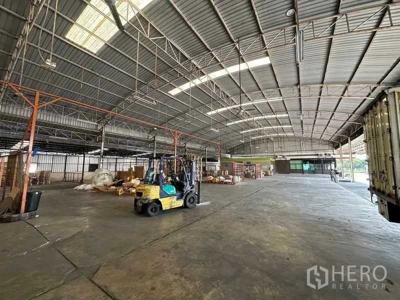 Warehouse for rent in Lam Luk Ka, Pathum Thani - Warehouse floor with forklift and goods beneath a metal truss roof.
