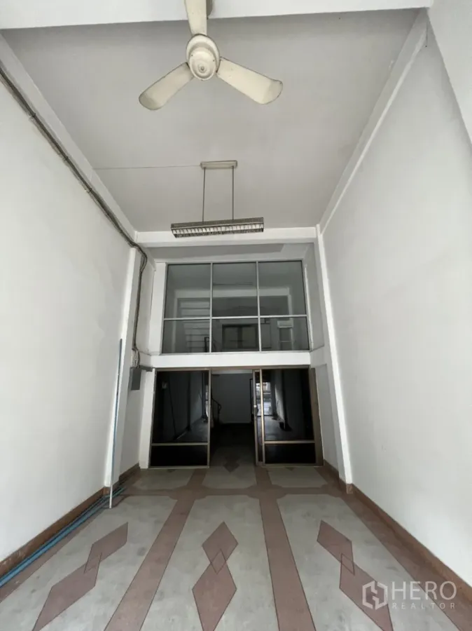Shophouse for rent in Phra Khanong, Bangkok - Empty shophouse ground floor with high ceiling, ceiling fan, patterned floor and glass mezzanine wall.