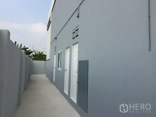 Warehouse for sale in Khlong Luang, Pathum Thani - Side service corridor beside gray warehouse with utility doors and a window.
