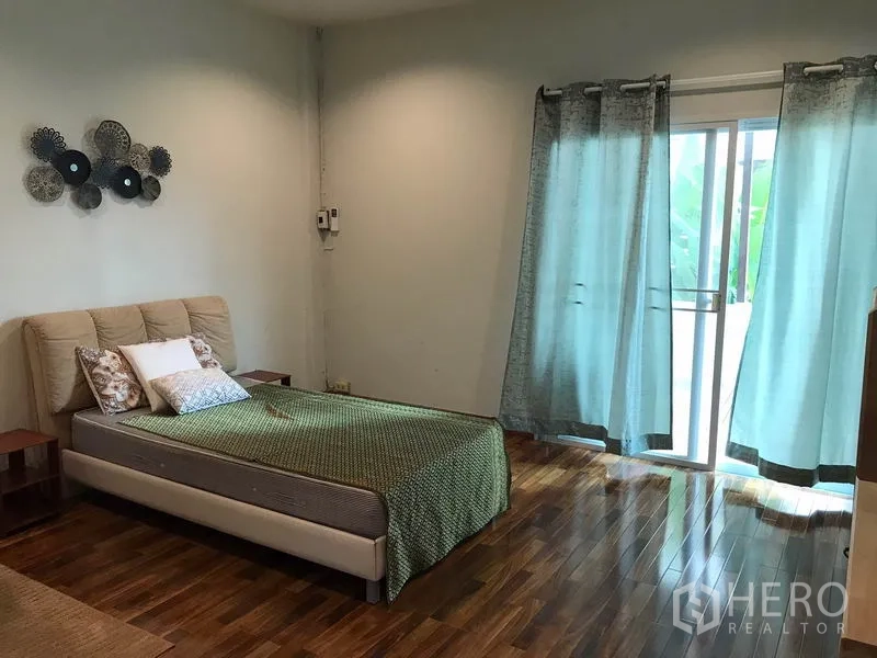 Townhouse for rent or sale in Phra Khanong, Bangkok - Spacious bedroom with wood floors and sliding glass doors opening to a balcony.