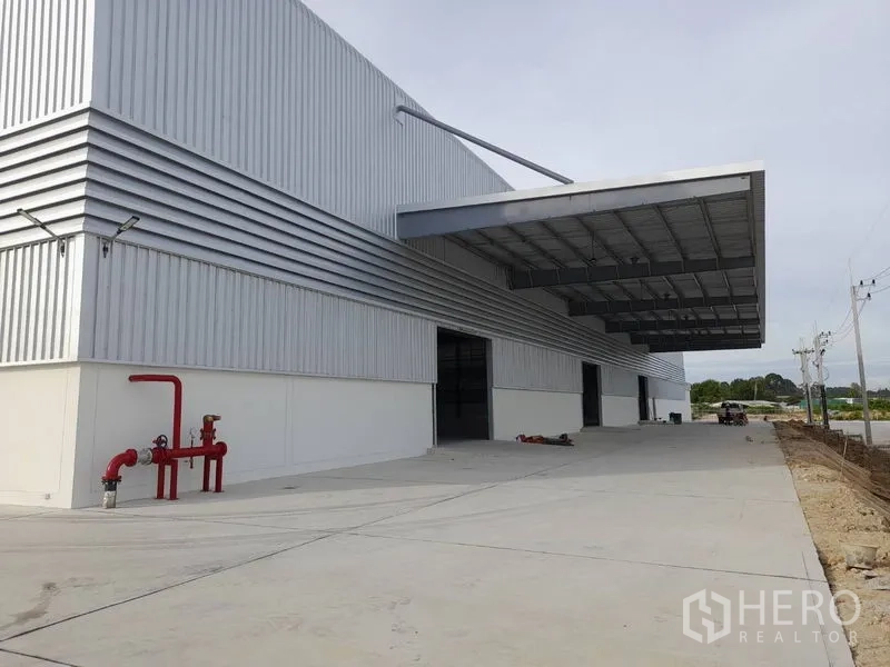 Factory for rent in Mueang Rayong, Rayong - Modern steel-clad factory exterior with large covered loading bay, wide concrete yard, and red fire hydrant system.