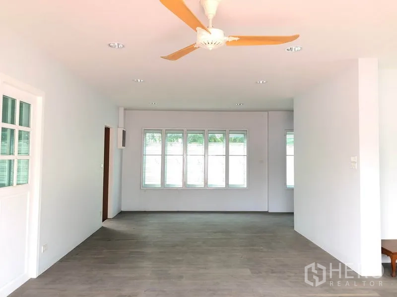 Detached House for sale in Bang Khen, Bangkok - Open-plan living area with wide windows, ceiling fan, grey wood-look floors and doors opening to the garden.