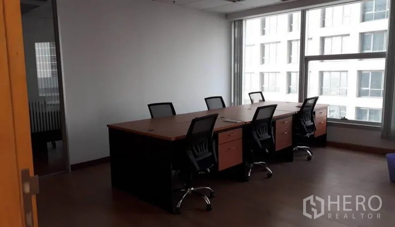Office Space for rent in Bang Rak, Bangkok - Meeting area with a large shared desk and office chairs beside a wide window overlooking a neighboring building.