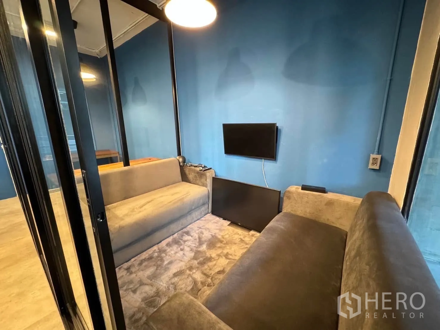 Home Office for rent in Watthana, Bangkok - Compact private meeting booth with two sofas and a wall-mounted TV behind glass doors.