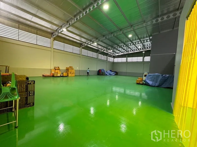 Factory for rent or sale in Lam Luk Ka, Pathum Thani - Open production space with high truss roof, bright lighting and green epoxy flooring.