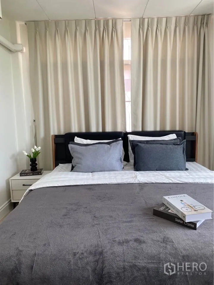 Detached House for rent in Huai Khwang, Bangkok - Cozy bedroom with bed, bedside tables and full-length curtains.