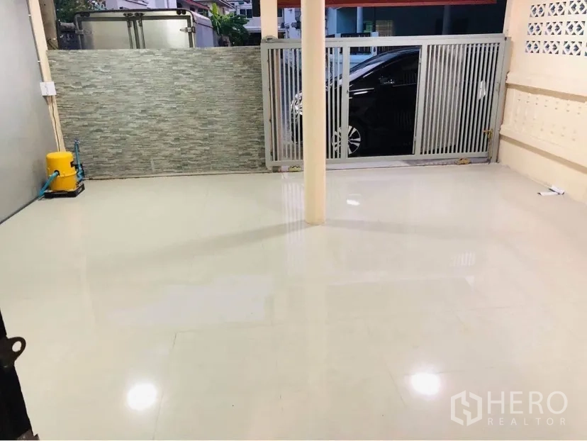 Townhouse for rent or sale in Huai Khwang, Bangkok - Covered carport with tiled floor, sliding gate and stone accent wall.