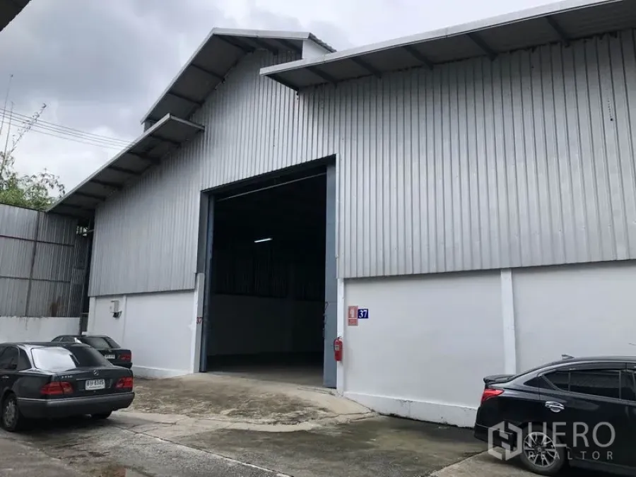 Warehouse for rent in Pak Kret, Nonthaburi - Steel-clad warehouse facade with a large loading entrance and parking area in Pak Kret.