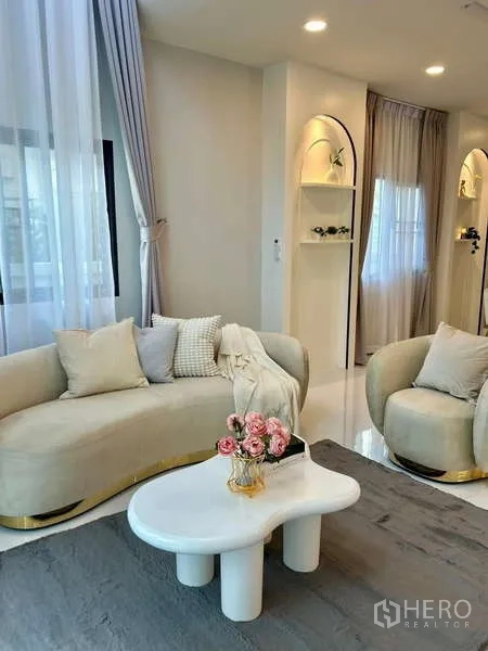 独立式住宅 出租在Bang Phli, Samut Prakan - 优雅客厅，弧形沙发、纱帘与雕塑感白色茶几。