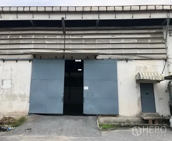Warehouse for rent in Bang Phli, Samut Prakan - Warehouse exterior with a large sliding steel door, loading ramp, and side personnel door.