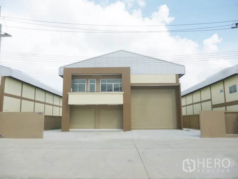 Factory for sale in Pathum Thani - Modern factory facade with large roller shutter and office windows in a gated industrial estate.