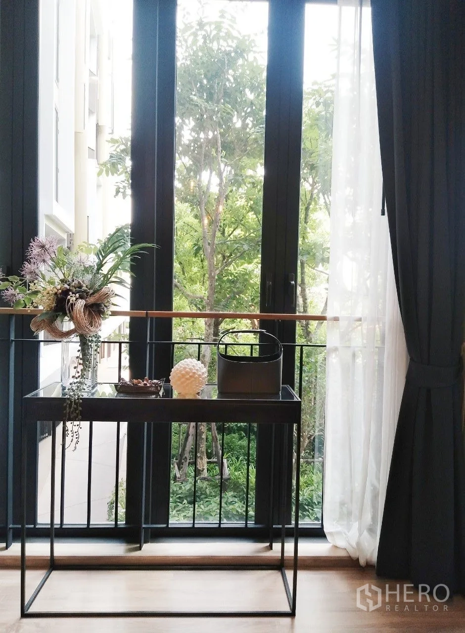 Condominium for rent in Watthana, Bangkok - Tall window nook with a console table overlooking lush green trees.