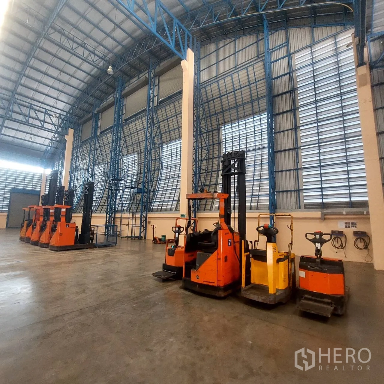 Warehouse for rent in Mueang Pathum Thani, Pathum Thani - Electric forklifts and pallet jacks parked under tall steel truss walls inside the warehouse.