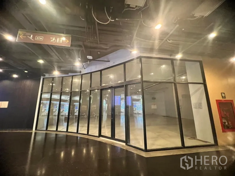 Retail Space for rent in Watthana, Bangkok - Curved glass shopfront along an indoor mall corridor with exposed ceiling and bright lighting.