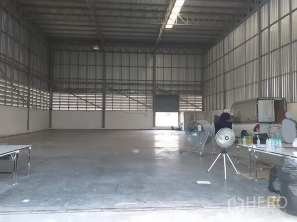 Warehouse for rent in Pak Kret, Nonthaburi - Spacious warehouse interior with a high steel roof, skylight strip, roller shutter, and smooth concrete floor.