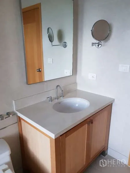 Condominium for rent - Close-up of bathroom vanity with countertop sink, mirror and wall-mounted magnifying mirror.