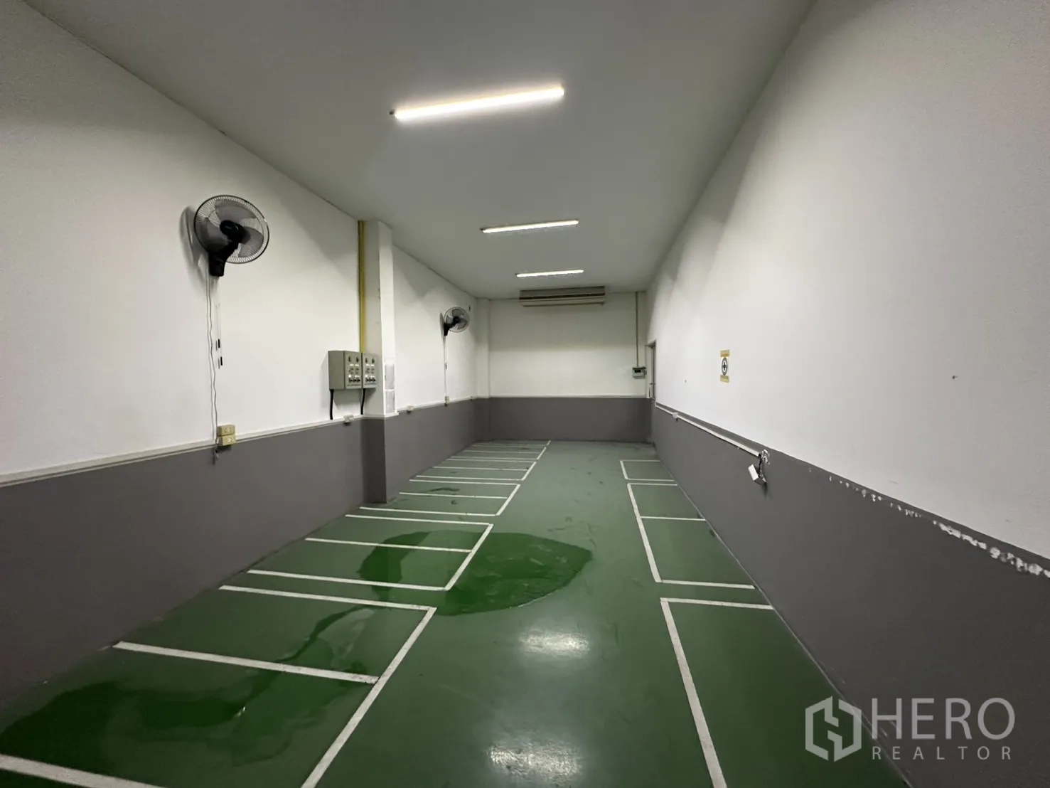 Factory for rent - Narrow green-floored room with wall fans and marked work bays.