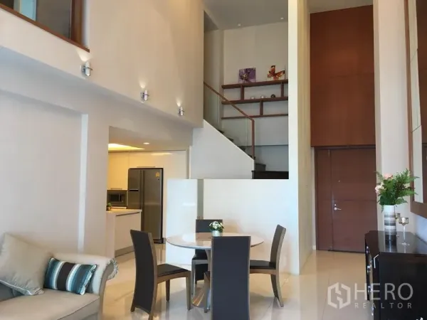 Condominium for rent in Pathum Wan, Bangkok - Double-height living space with staircase to a mezzanine, open kitchen and dining set.