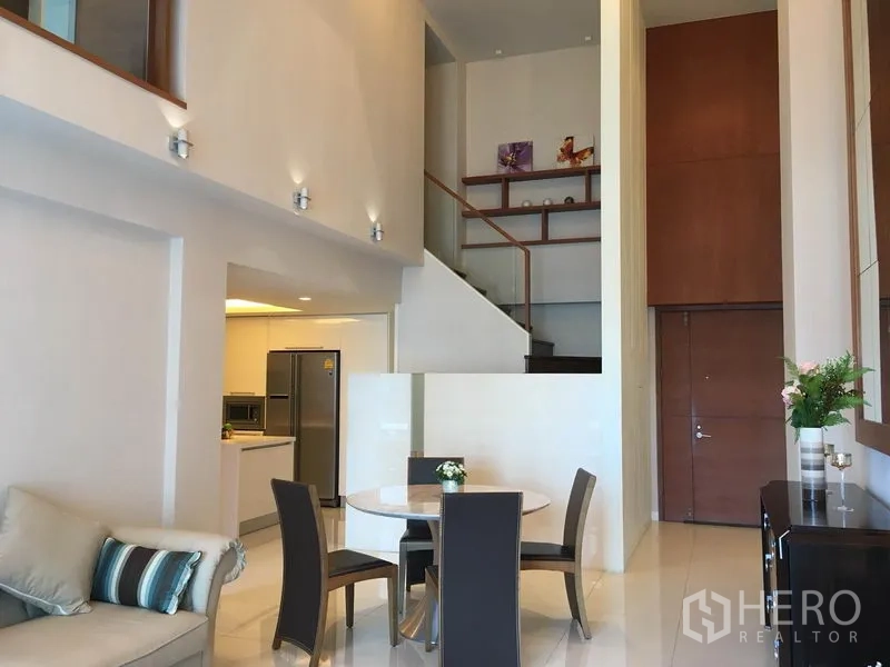 Condominium for rent in Pathum Wan, Bangkok - Double-height living space with staircase to a mezzanine, open kitchen and dining set.