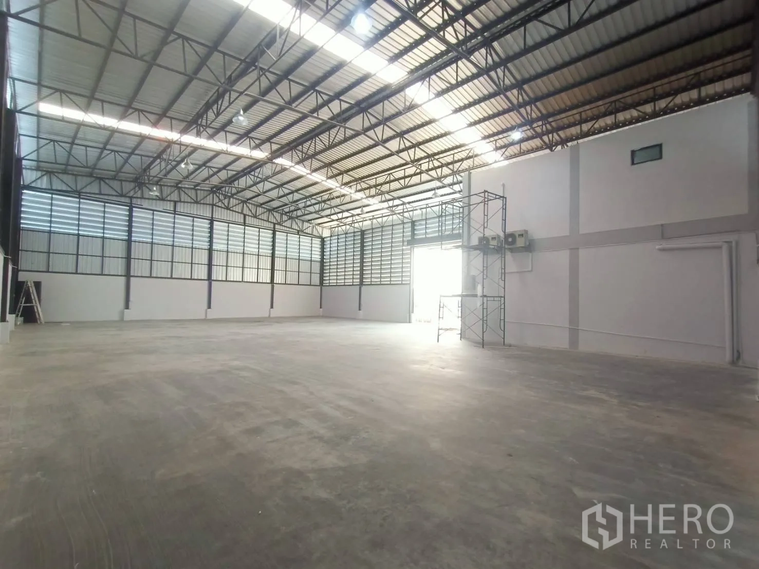 Factory for rent or sale in Mueang Samut Sakhon, Samut Sakhon - Spacious factory hall with high steel truss roof, polished concrete floor, and louvered wall panels for ventilation and daylight.
