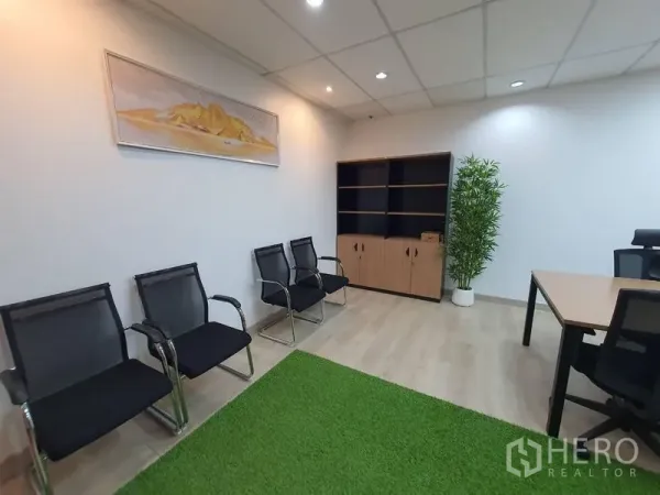 Office Space for rent - Waiting area with three black mesh chairs, wood shelving unit and potted plant beside a work desk.