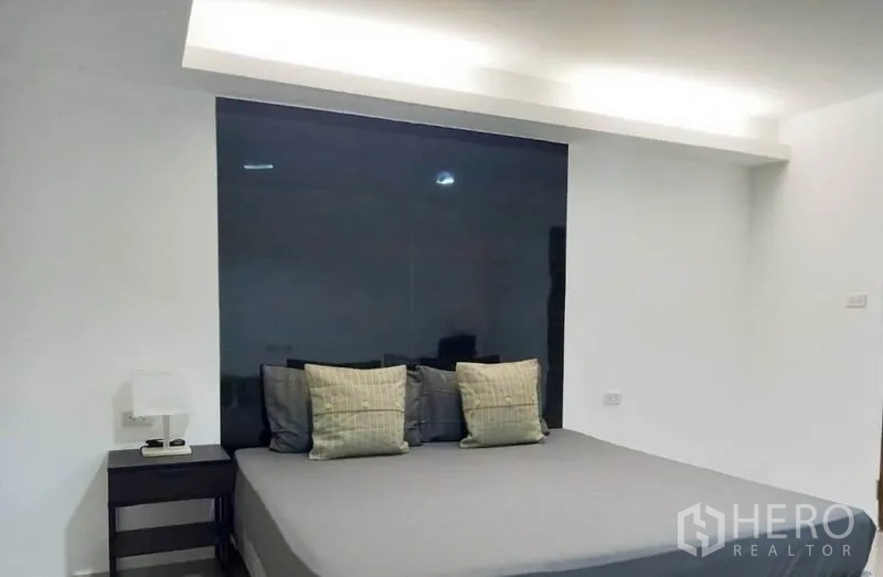 Condominium for rent in Khlong Toei, Bangkok - Bedroom with a king-size bed, dark feature wall and bedside table.