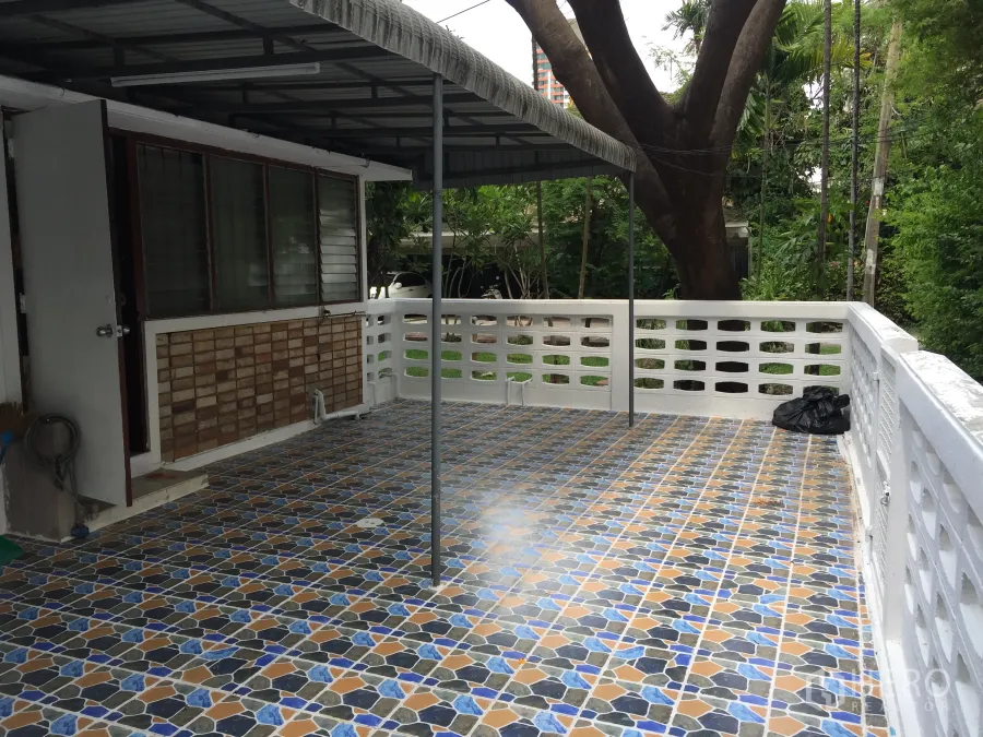 联排别墅 出租在Yan Nawa, Bangkok - 带遮阳棚的彩色瓷砖露台，白色栏杆，面向绿意花园。