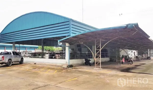 Factory for sale in Lam Luk Ka, Pathum Thani - Open‑sided steel canopy and yard area with parking for vehicles and motorbikes.