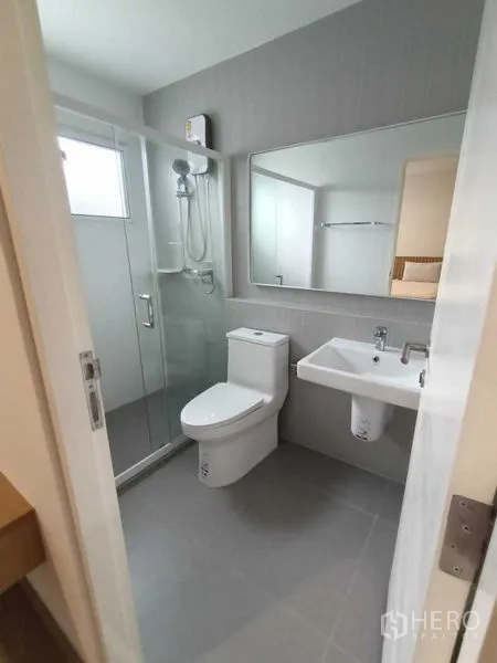 Townhouse for rent in Prawet, Bangkok - Modern bathroom with glass-enclosed shower, toilet and large mirror above the sink.