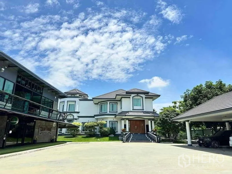 Detached House for sale in Khlong Luang, Pathum Thani - Front elevation of the house with wide steps, manicured garden, and separate carport.