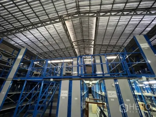 Warehouse for rent in Khlong Toei, Bangkok - Two-tier mezzanine racking with stair access beneath a steel truss roof.