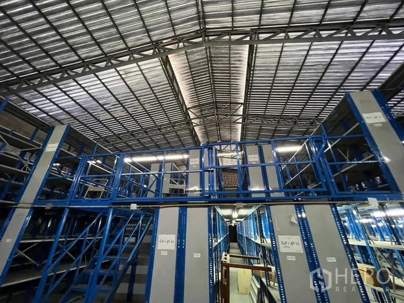 Warehouse for rent in Khlong Toei, Bangkok - Two-tier mezzanine racking with stair access beneath a steel truss roof.