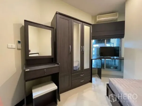 Apartment for rent in Khlong Toei, Bangkok - Compact bedroom with dark wood wardrobe, dressing table, TV desk and air conditioner.