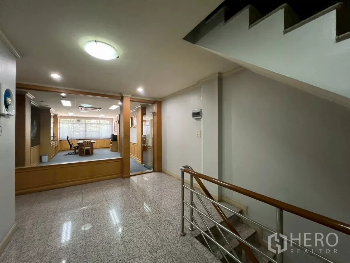 Shophouse for rent in Bang Rak, Bangkok - Hallway view toward an office room with glass doors and stainless stair railing.