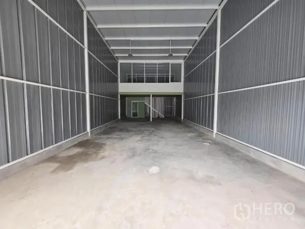 Warehouse for rent in Prawet, Bangkok - Spacious high-ceiling warehouse bay with concrete floor leading to a rear mezzanine office and staircase.