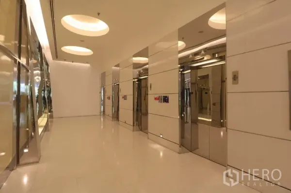 Office Space for rent in Bang Rak, Bangkok - Modern elevator lobby with multiple stainless-steel lifts and circular recessed ceiling lights.